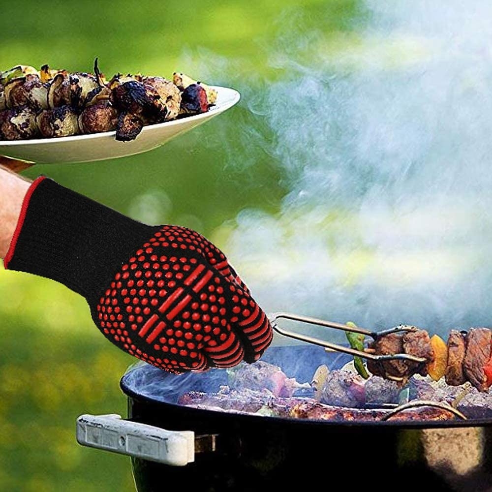 A hand protected by the non-slip, heat-resistant grilling gloves, holding kebab over the barbecue.