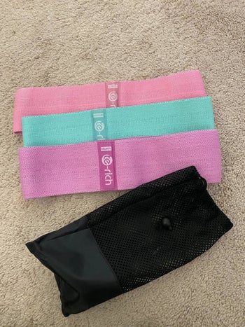 Reviewer image of the three bands in pastel pink, purple, and teal with the black bag that comes with it 
