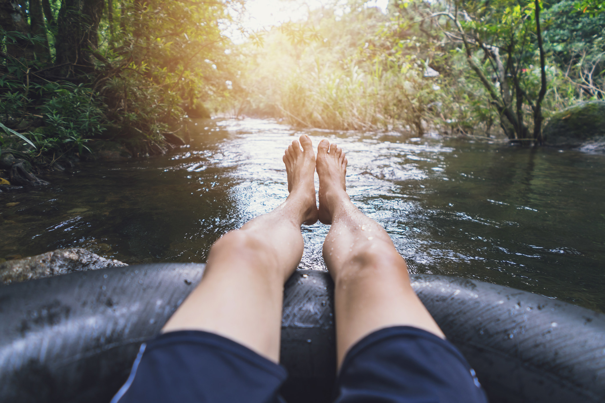 Person tubing down a river from a first-person POV. You see his feet and the river ahead.