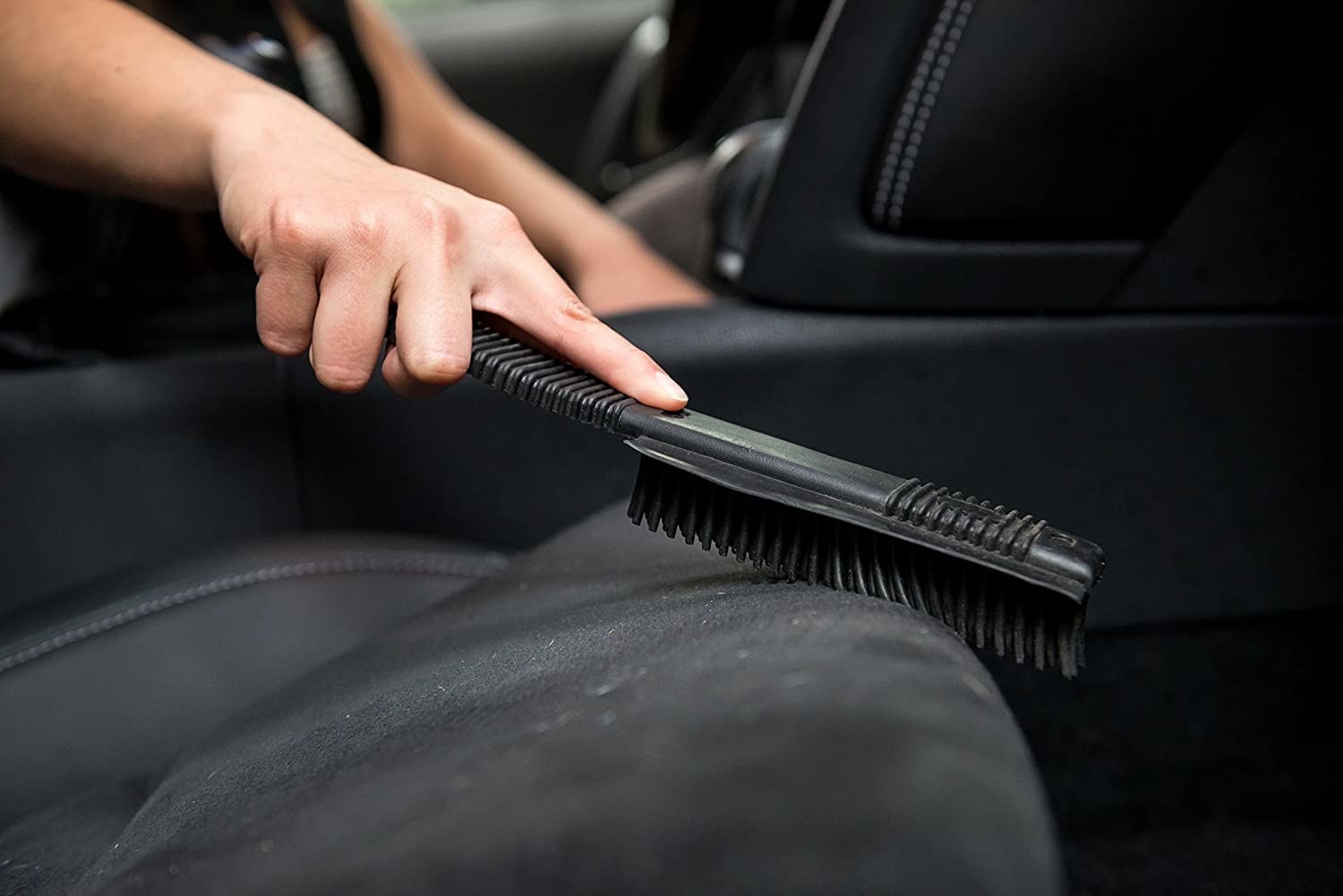 A close up of a person using the brush on dusty car seats