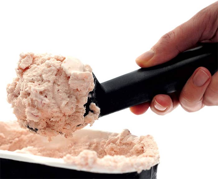 A person scoops ice cream out of a tub