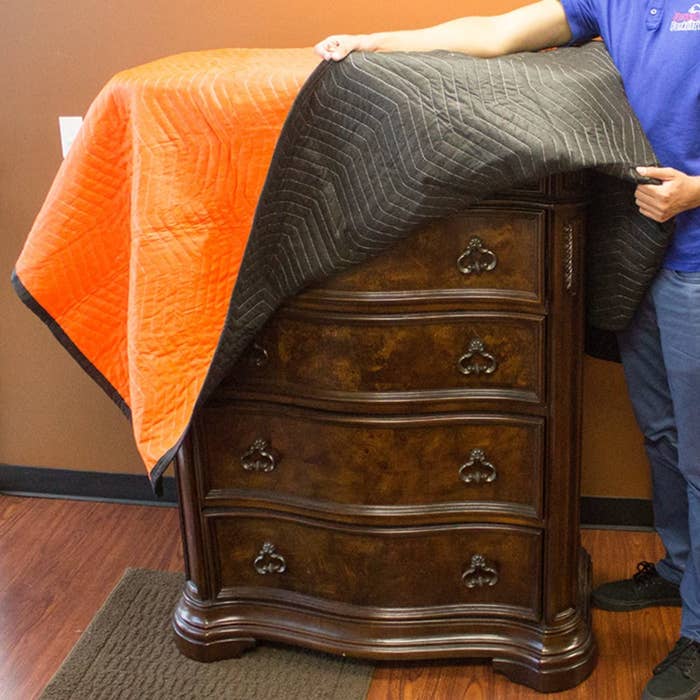A model covering a wooden chest of drawers with and orange and black moving blanket