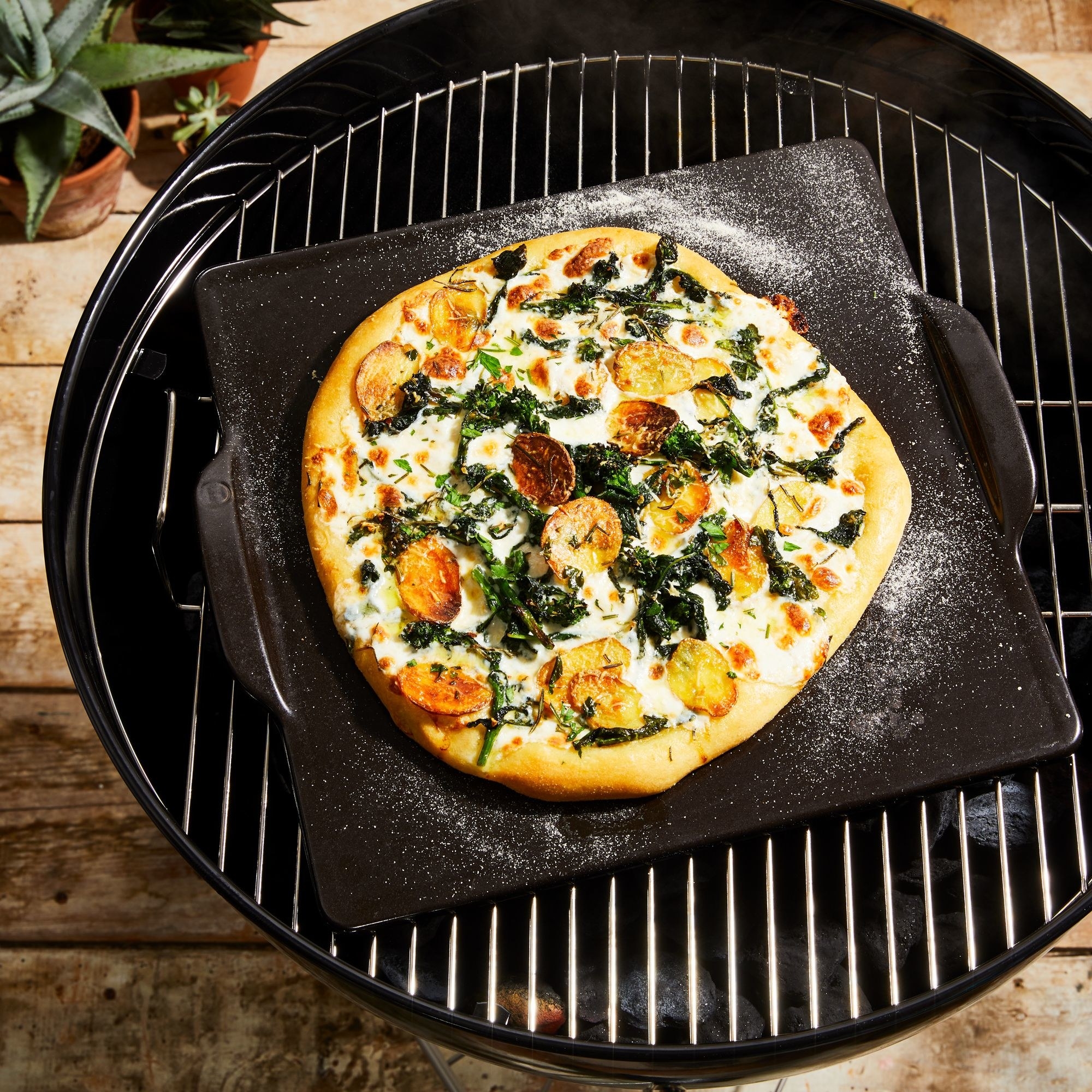 A pizza cooking on the ceramic pizza stone on a grill.