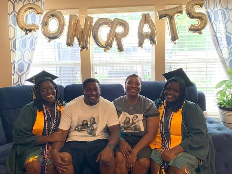 Photo of the twins and their parents on a couch with a sign saying "congrats" behind them.