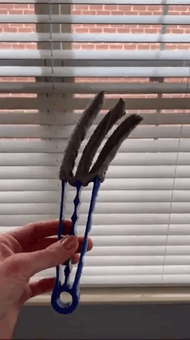 a gif of a person holding the duster brush and twisting it around. The brush is shaped similar to tongs but has three prongs instead of two