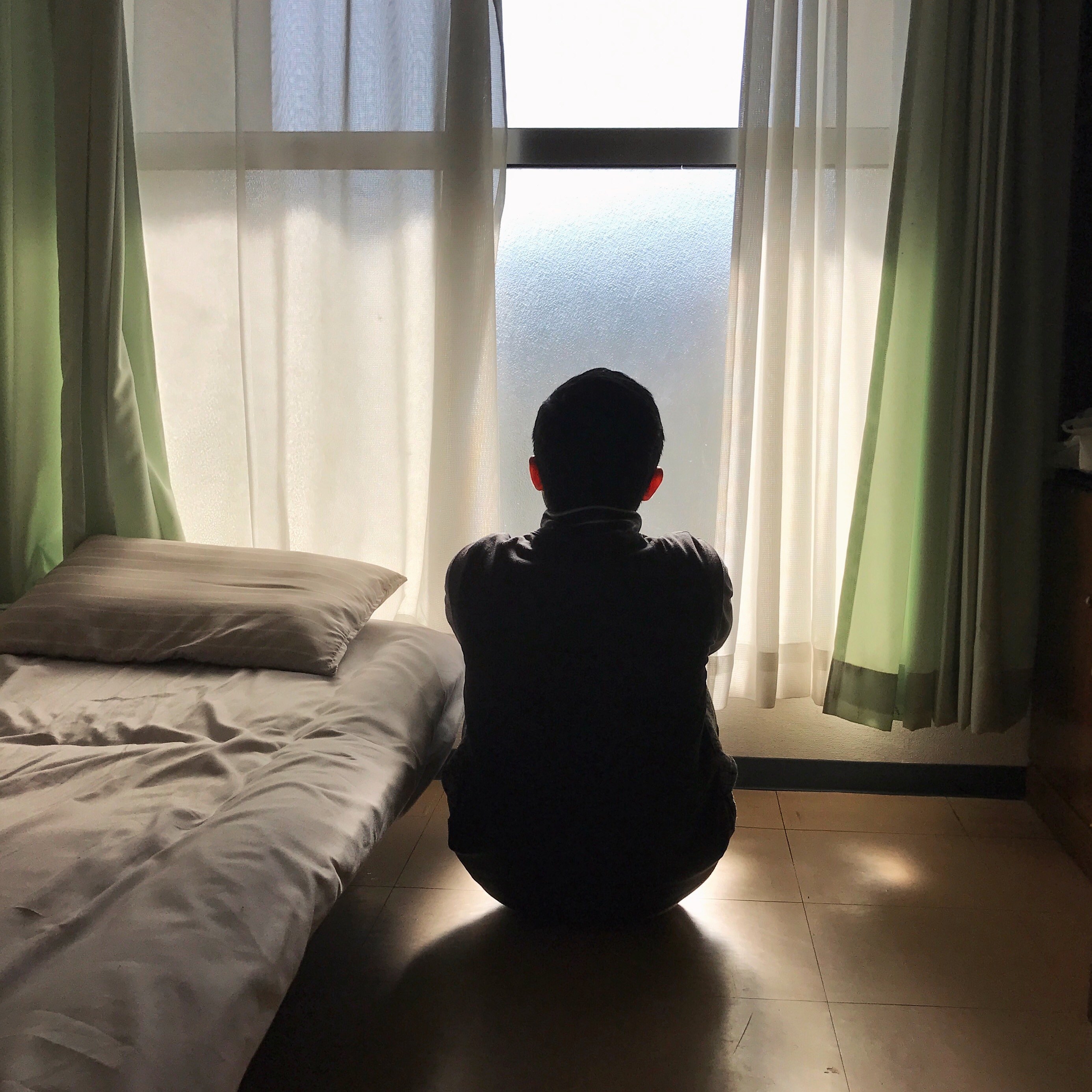 A boy looks out a window next to a bed