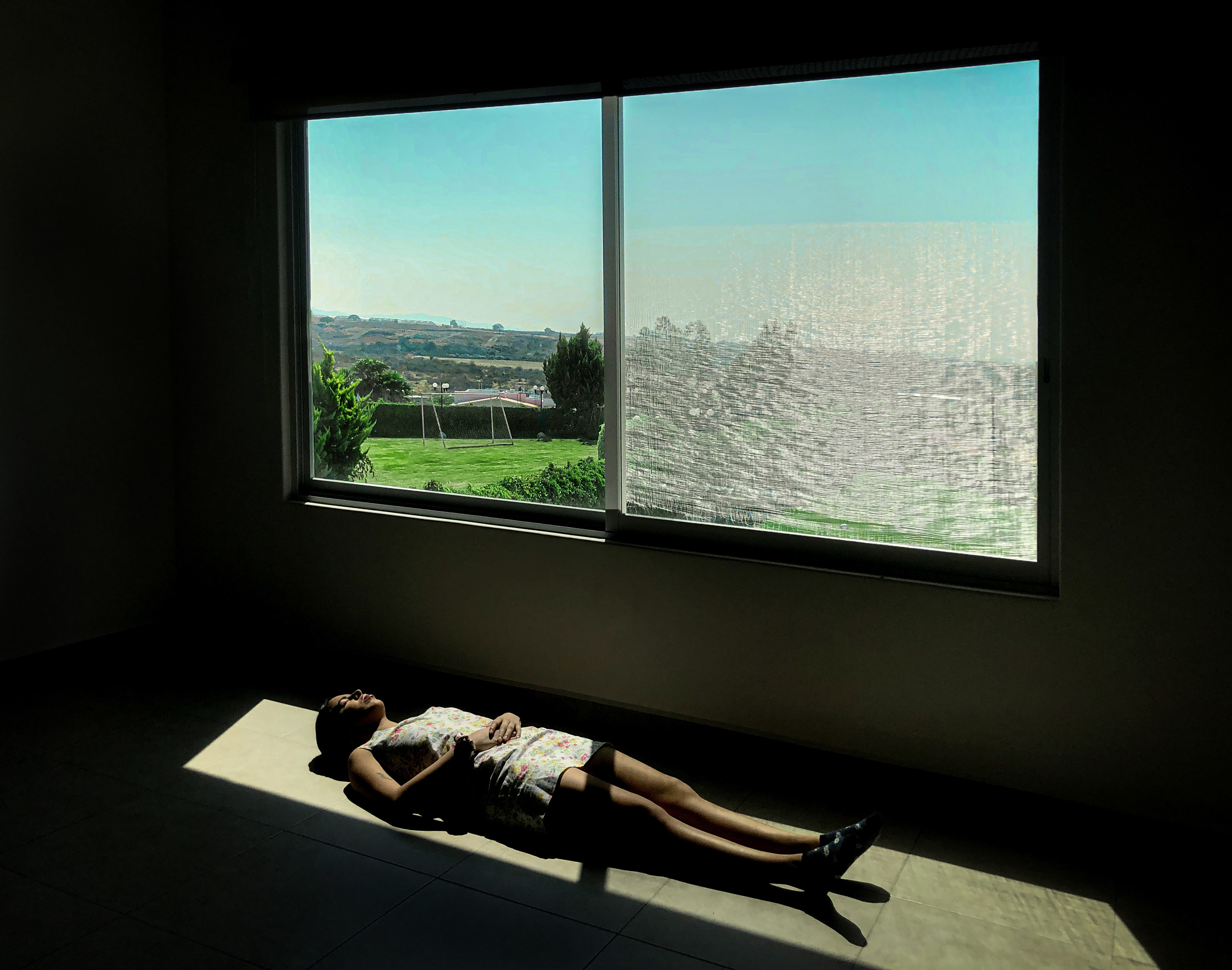 A woman lies on the floor in a patch of light next to a window