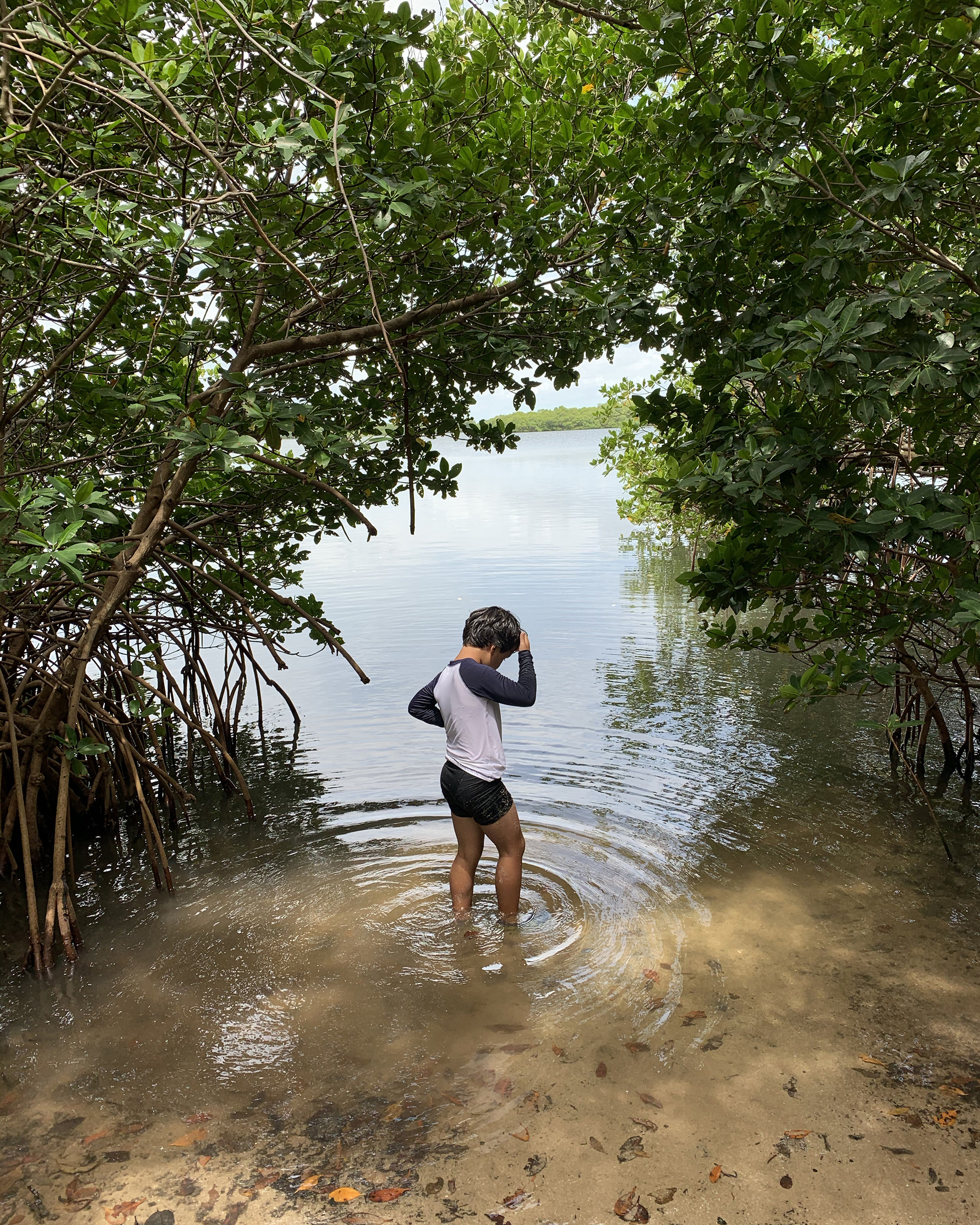 A boy scratches his head while standing in shallow water