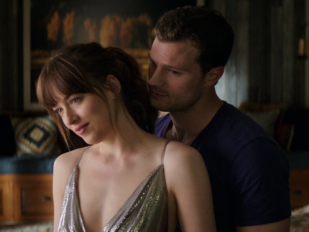 Jamie Dornan as Christian hugs Ana (Dakota Johnson) from behind. 