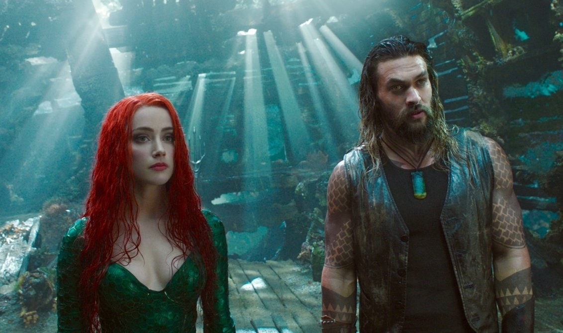 Jason Momoa as Aquaman stands side-by-side with Mera (Amber Heard) under water.