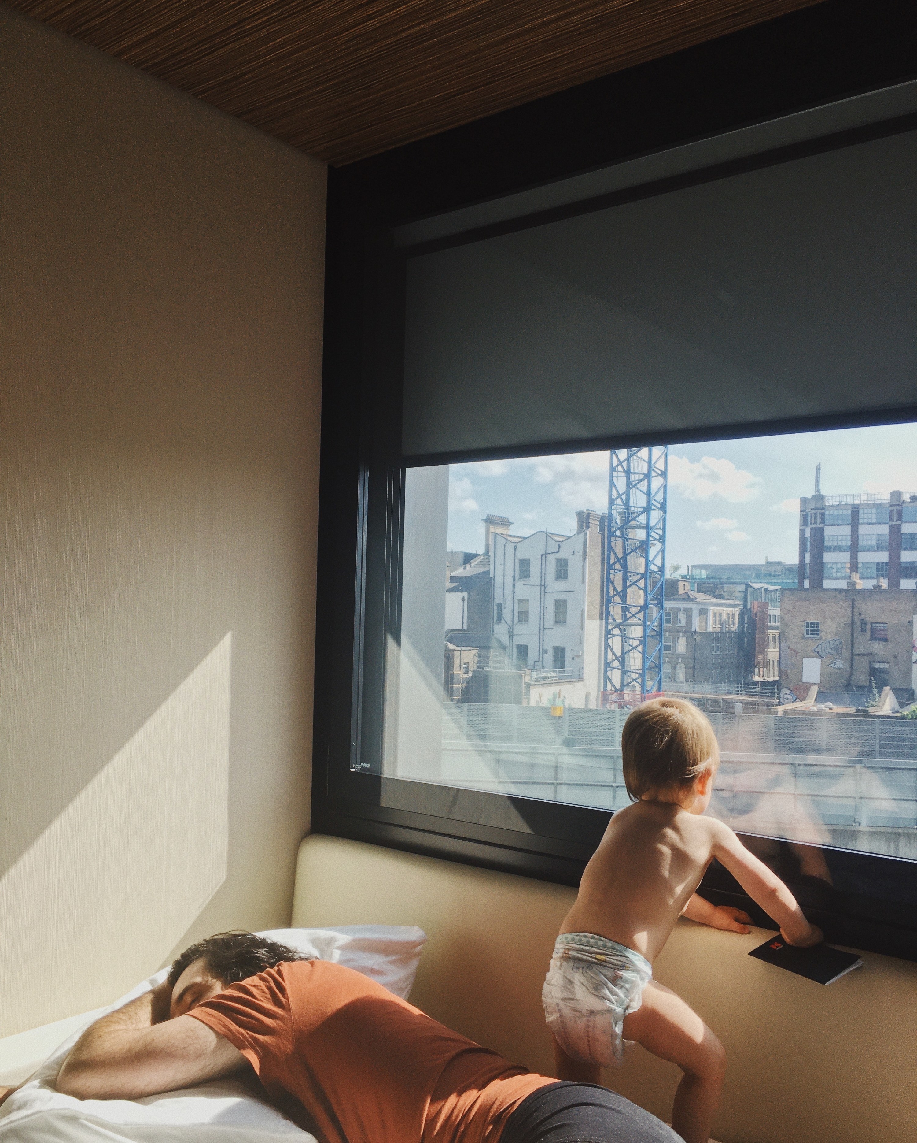 A father sleeps while his small child looks out a window overlooking a city
