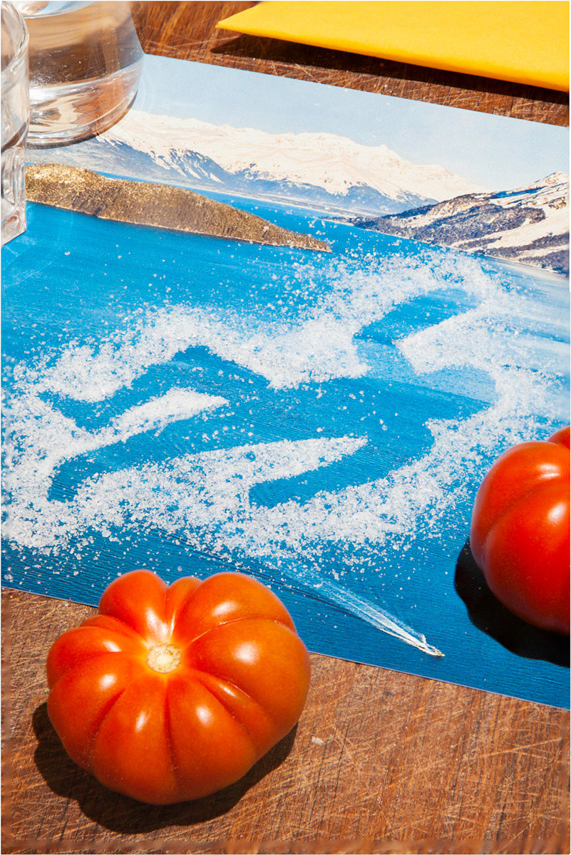 An outline of a person is drawn in salt on a cutting board next to tomatoes