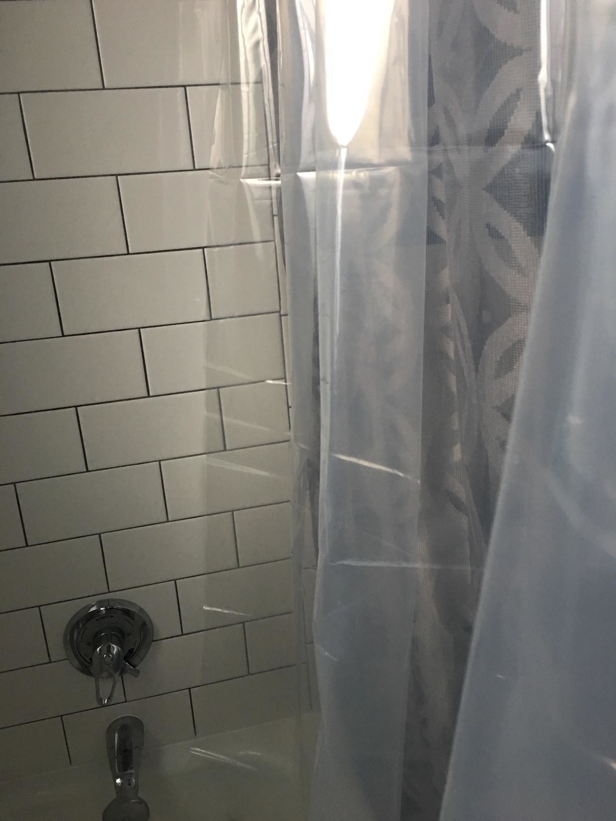 A reviewer's photo of a clear shower curtain in the bathroom