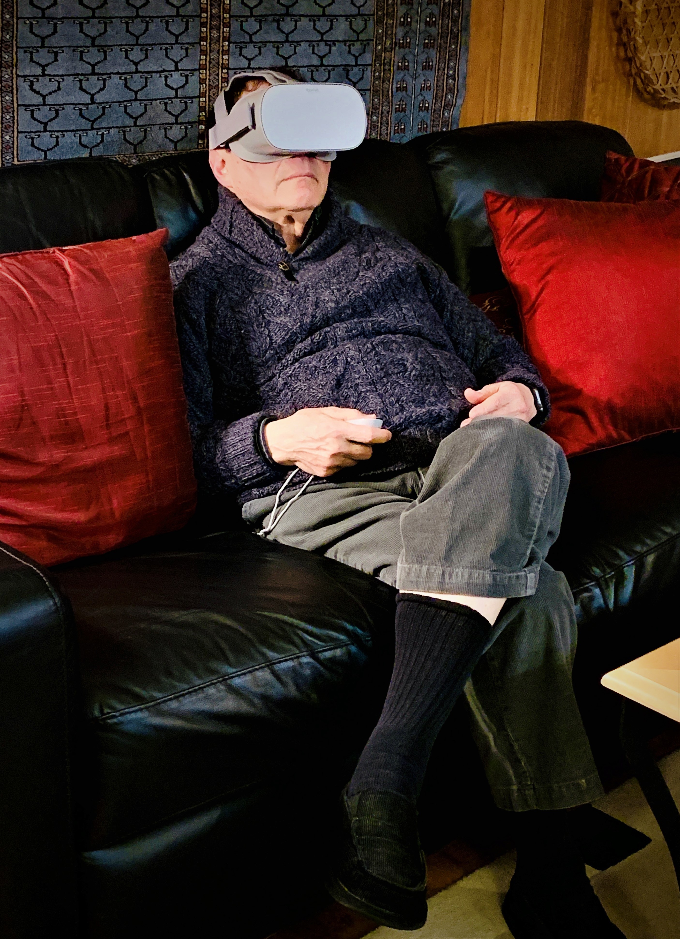 An older man wearing VR glasses sits on a couch