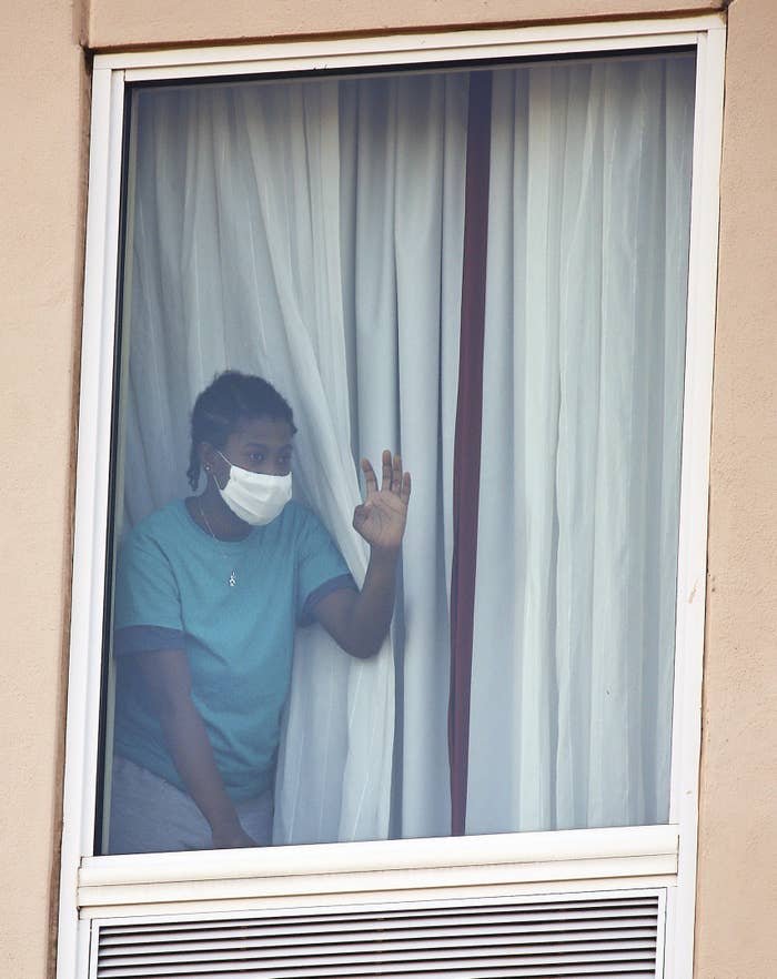 A girl wearing a face mask waves from a hotel room window