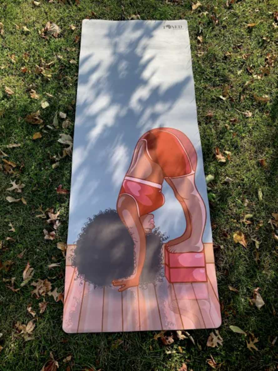 Yoga mat with an illustration of a woman standing on yoga blocks with her head full of curly hair on the ground in front of her
