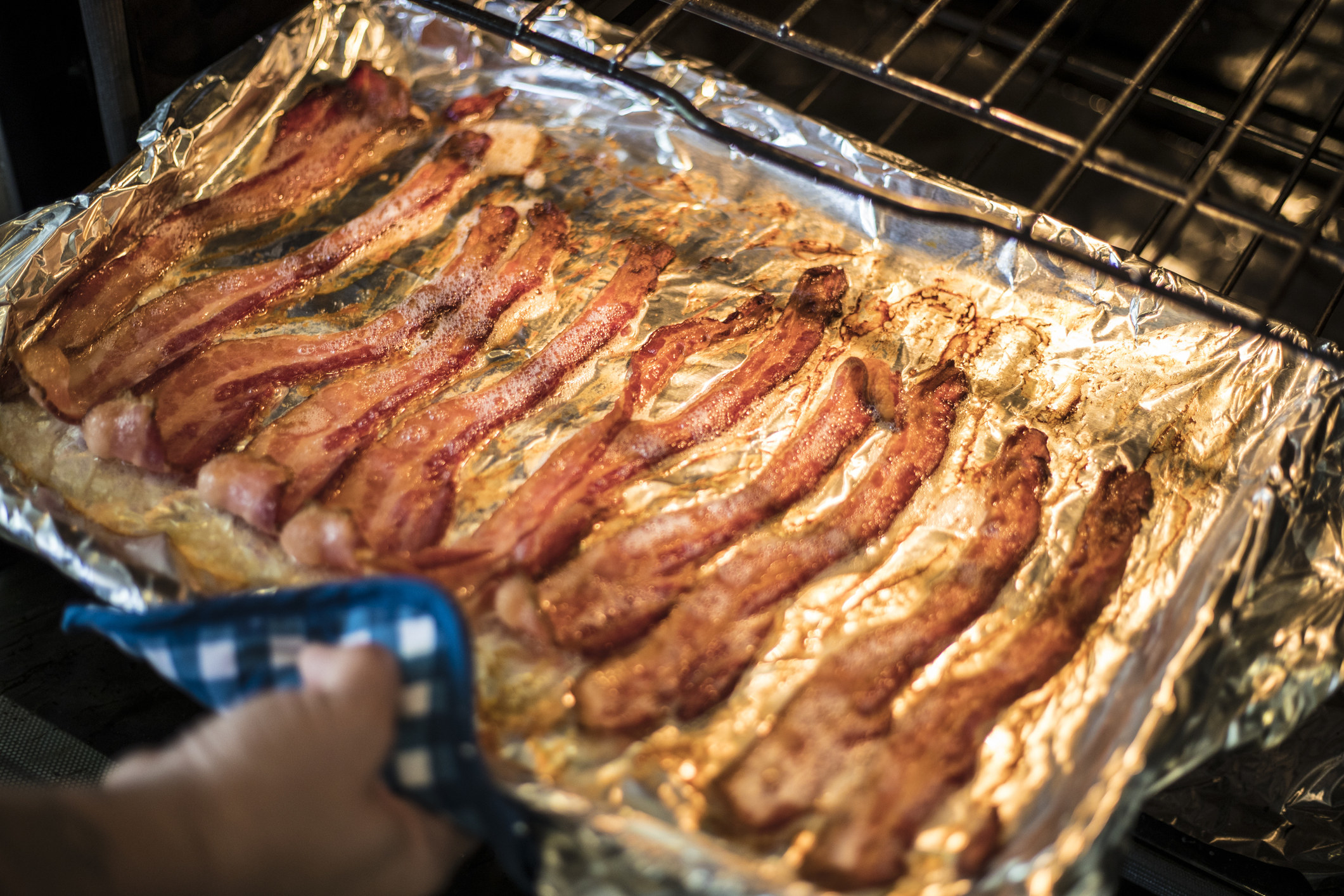 Someone removing a baking sheet topped with bacon from the oven.