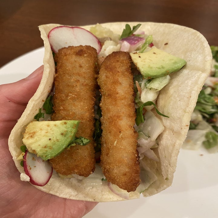 A tortilla filled with slaw, avocado, and two fish sticks.