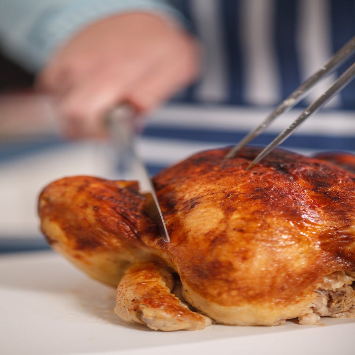 Someone slicing a rotisserie chicken on a cutting board.