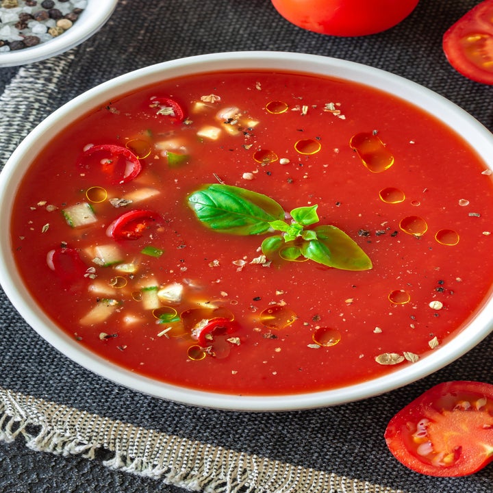 A bowl of gazpacho with diced tomato and cucumbers on a table.