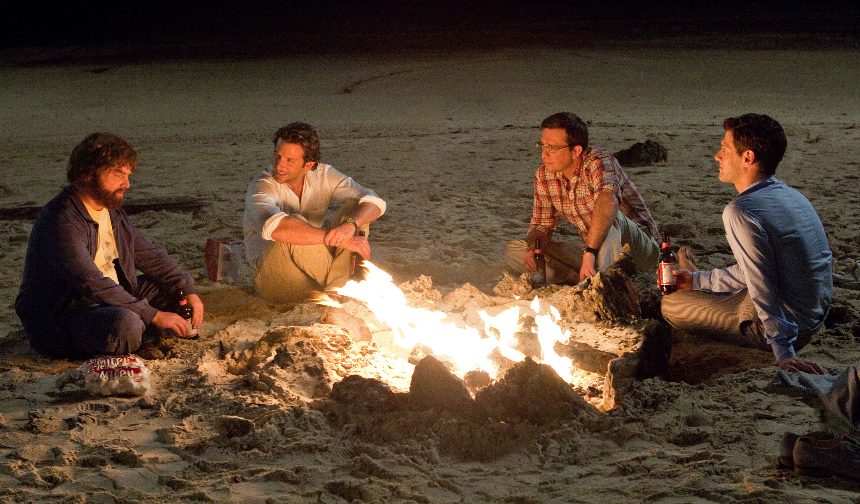 A still from the movie The Hangover shows the four guys on the beach sitting around a small bonfire