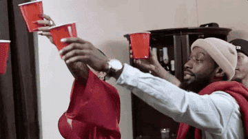 Several people at a house party raise their red solo cups to toast one another