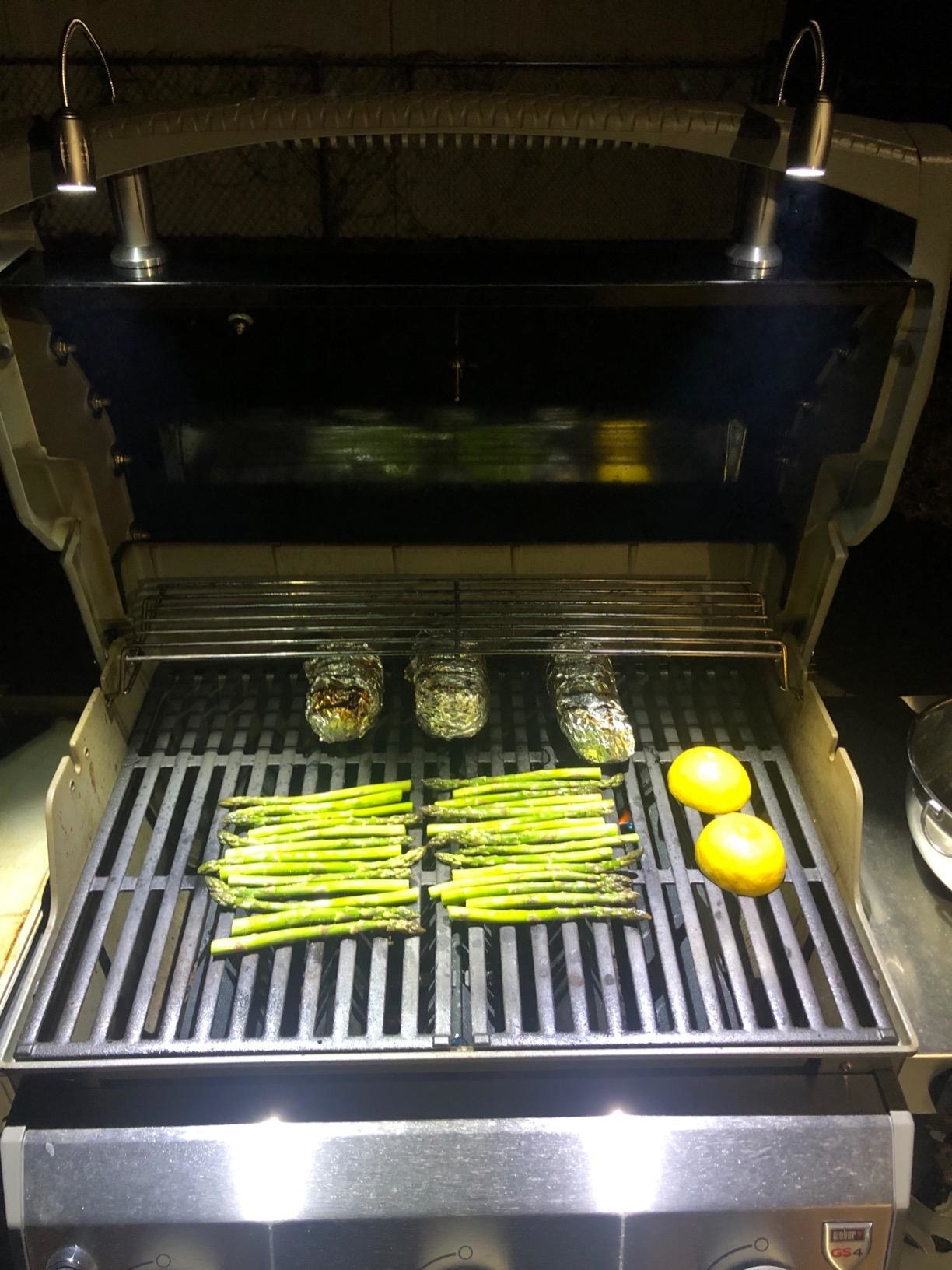A barbecue with skewers and vegetables cooking, lit up by a pair of magnetic lights at night.