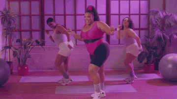 gif of Lizzo in the video for her song &quot;Juice&quot; in 80s workout gear and dancing with two people behind her