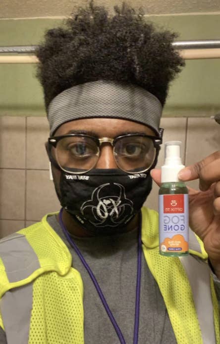 A reviewer image of a person wearing unfogged glasses with their face mask holding up the spray 