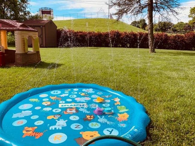 A blue circular splash pad with colorful animals and letters spraying water all around