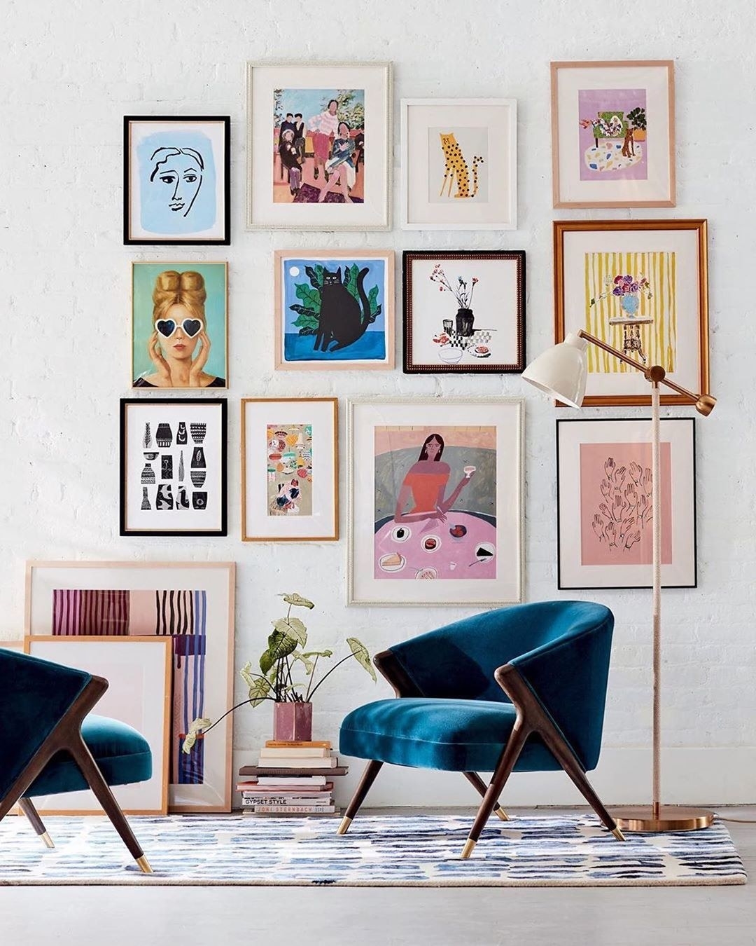 A simple gallery wall extends from the floor to ceiling behind two armchairs and a lamp