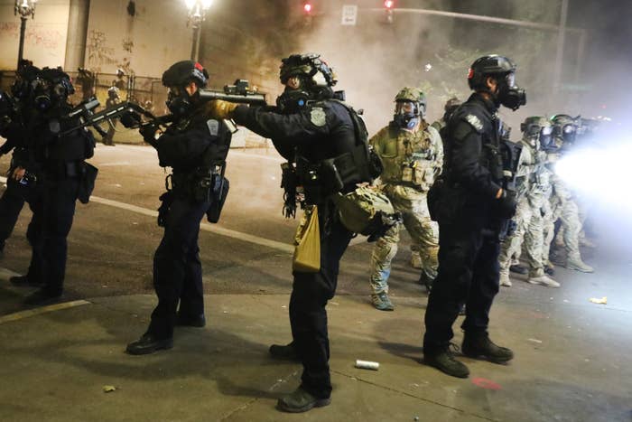 Federal officers dressed in all black with helmets and gas masks aim their weapons