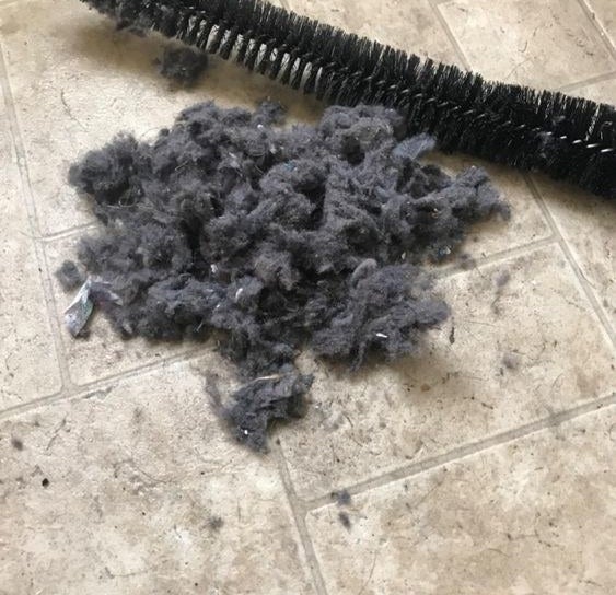 Reviewer&#x27;s picture of the vent-cleaning brush next to a large pile of lint