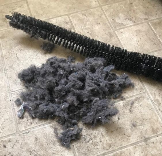 Reviewer&#x27;s picture of the vent-cleaning brush next to a large pile of lint