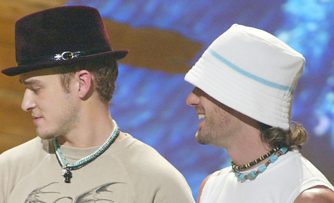 A photo of Justin Timberlake and JC Chasez on stage at each wearing several shell and beaded necklaces. 