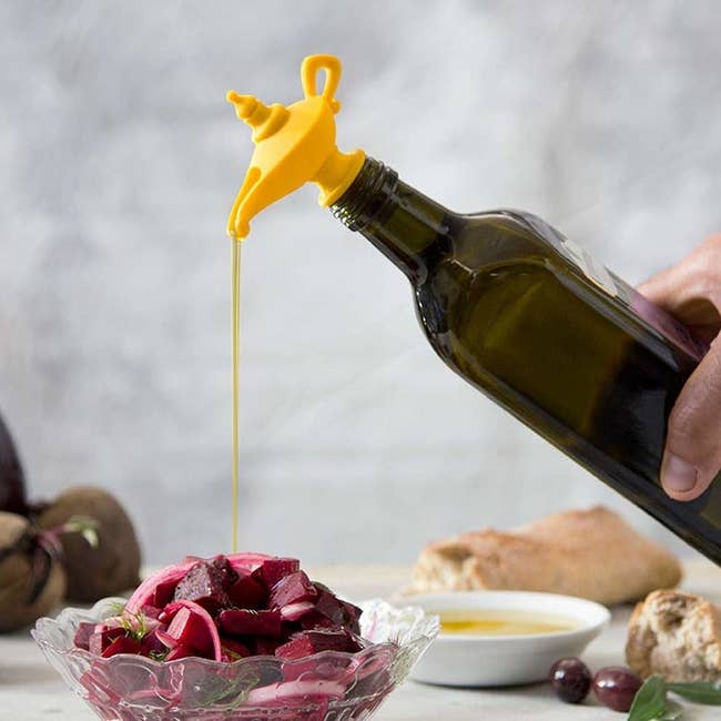 The stopper that looks like a genie lamp in yellow on top of a bottle of olive oil with some pouring out
