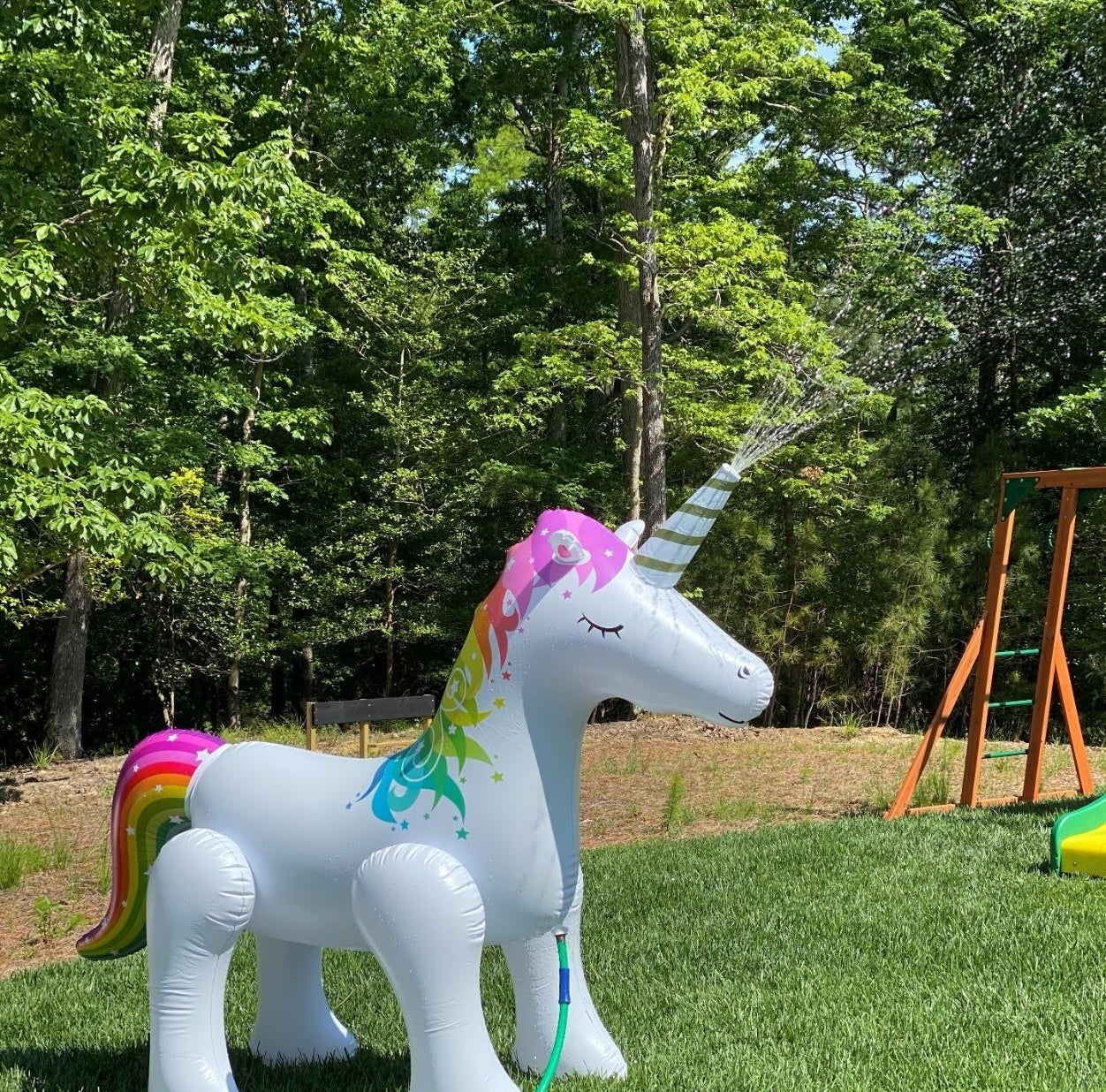 A white inflatable unicorn with multi-colored tail and mane spraying water from its horn 
