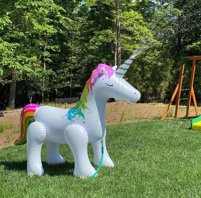 A white inflatable unicorn with multi-colored tail and mane spraying water from its horn 