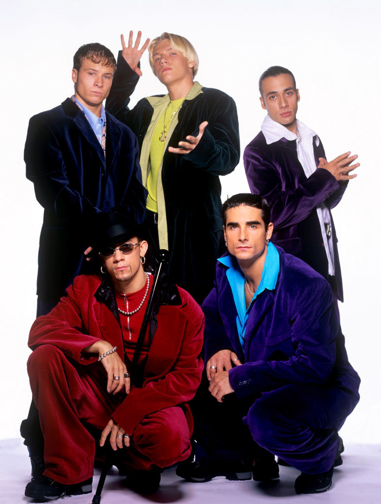 A photo of the Backstreet Boys in velvet suits with Nick Carter making magic hands.