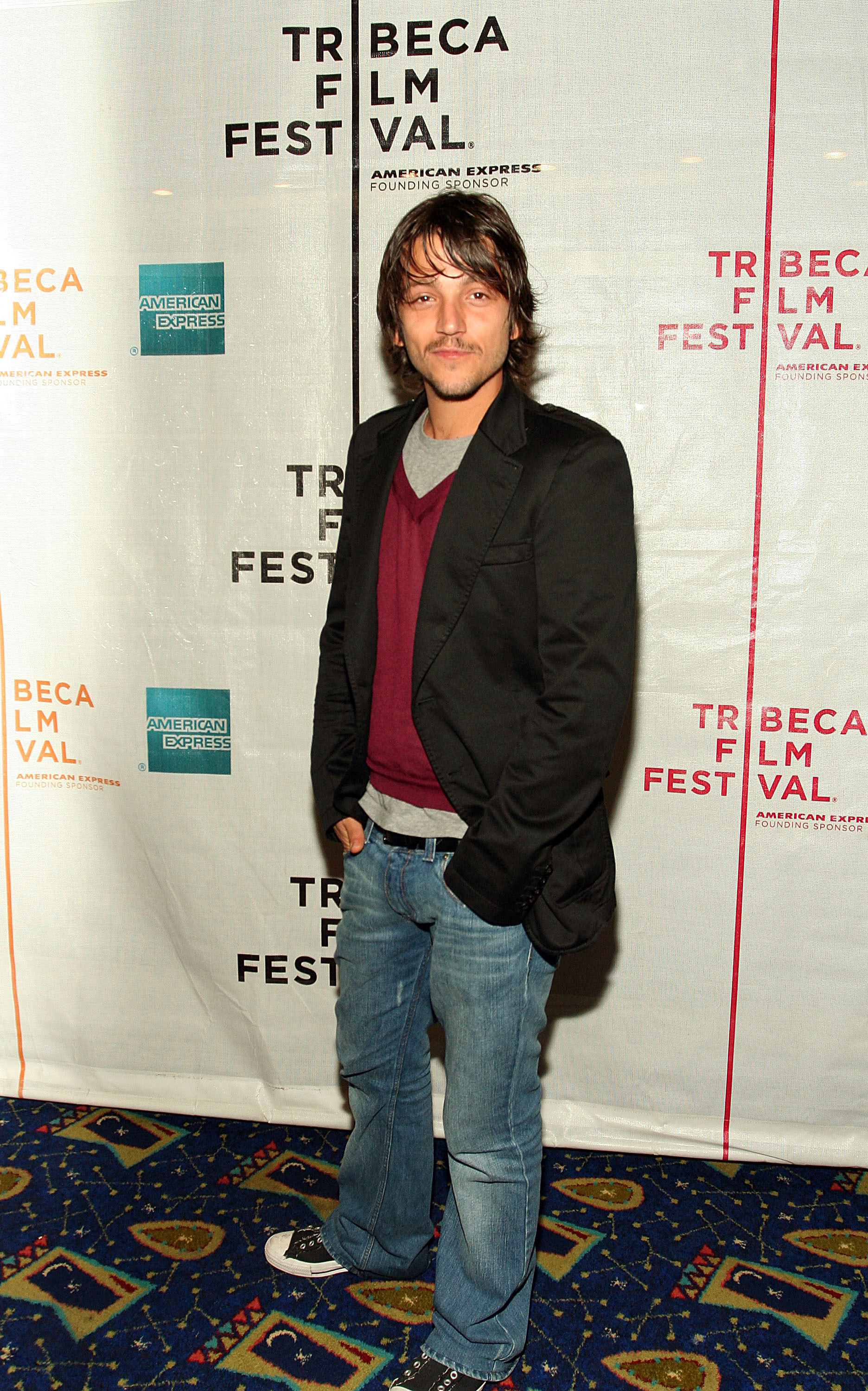 Diego Luna wearing bootcut jeans and black Converses.