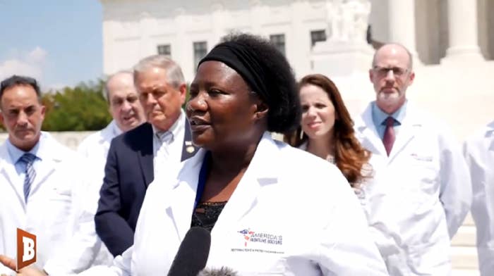 Doctors in white coats stand outside a building in front of a microphone