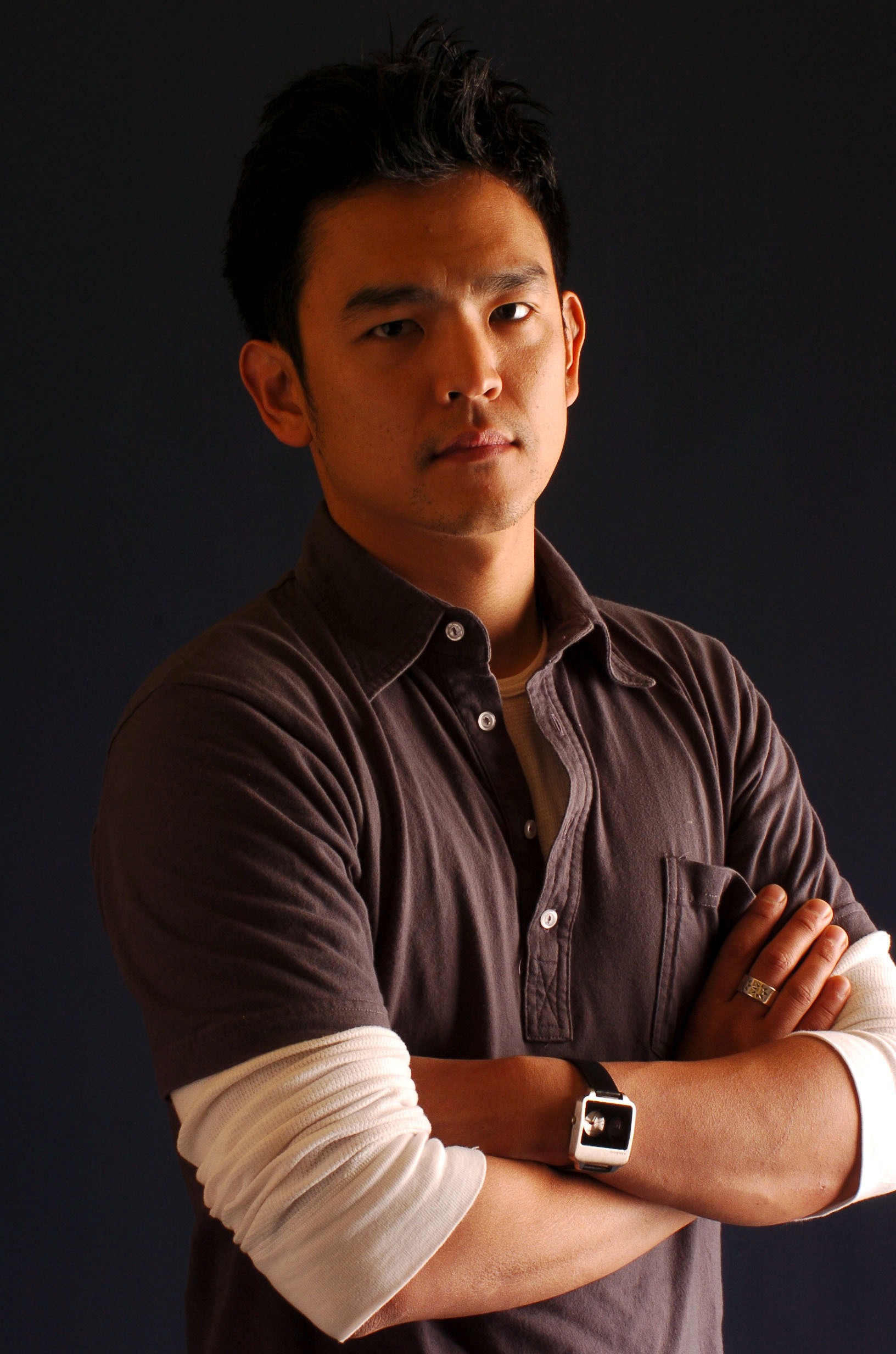 A photo of John Cho wearing a white thermal underneath a dark gray polo.