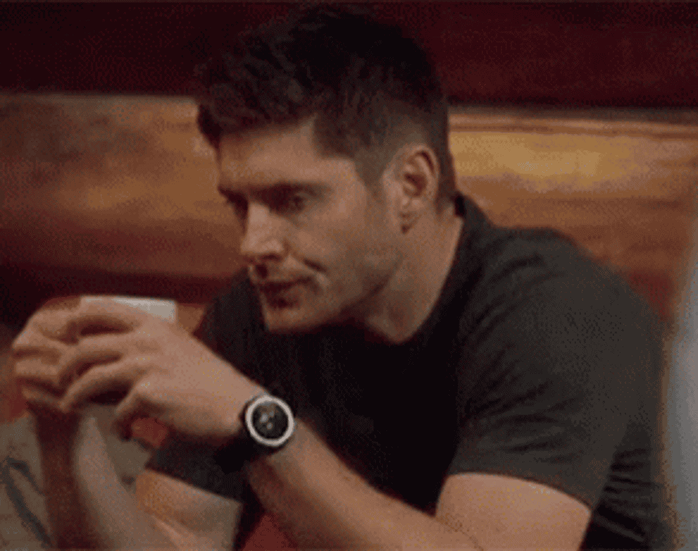 Dean holds his finger up to indicate the person talking to him should be quiet and then points to his coffee cup