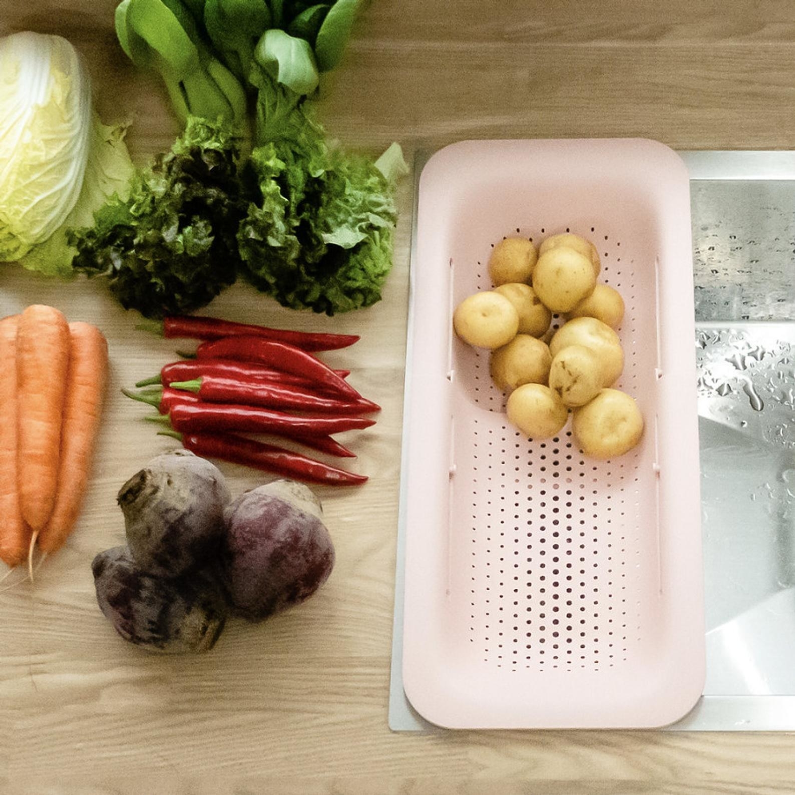 The strainer in pink expanded  to fit in a sink with potatoes in it and other vegetables next to it