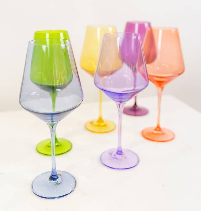 Six wine glasses; one in blue, purple, orange, green, yellow, and pink