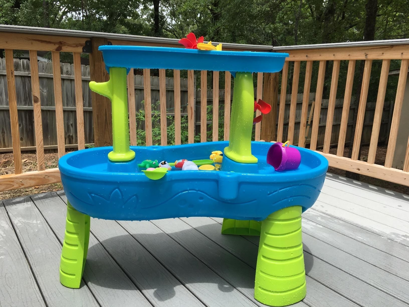 A teal and lime green water table with two levels and multi-colored toys inside