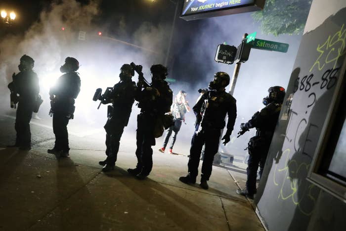 Six armed federal officers are seen in silhouette, white smoking illuminated behind them