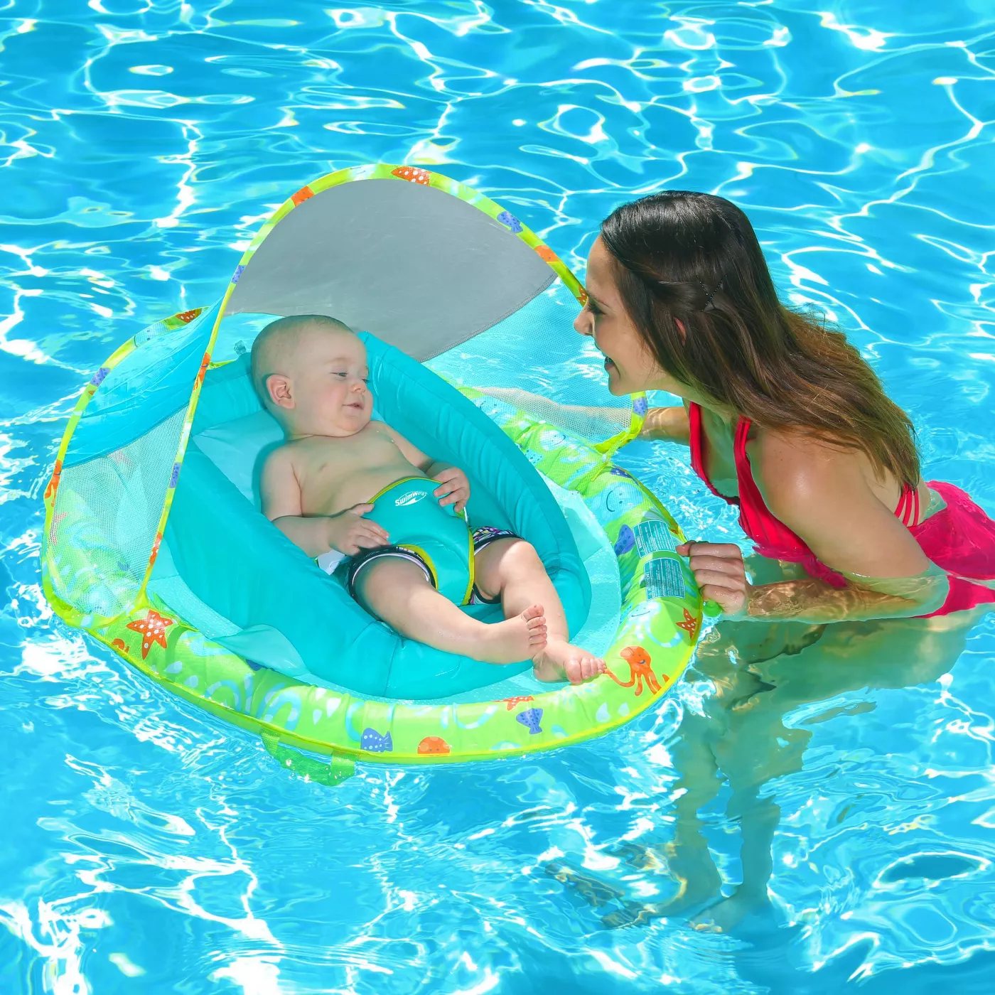 A baby model in a green- and teal-colored float with an adult model supervising