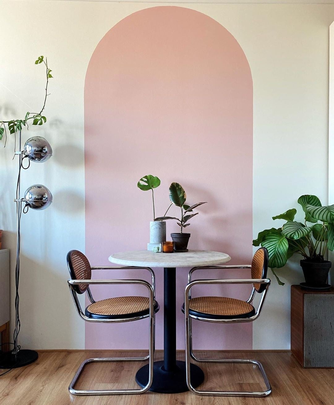 A pink archway is painted on a white wall behind a table and two chairs