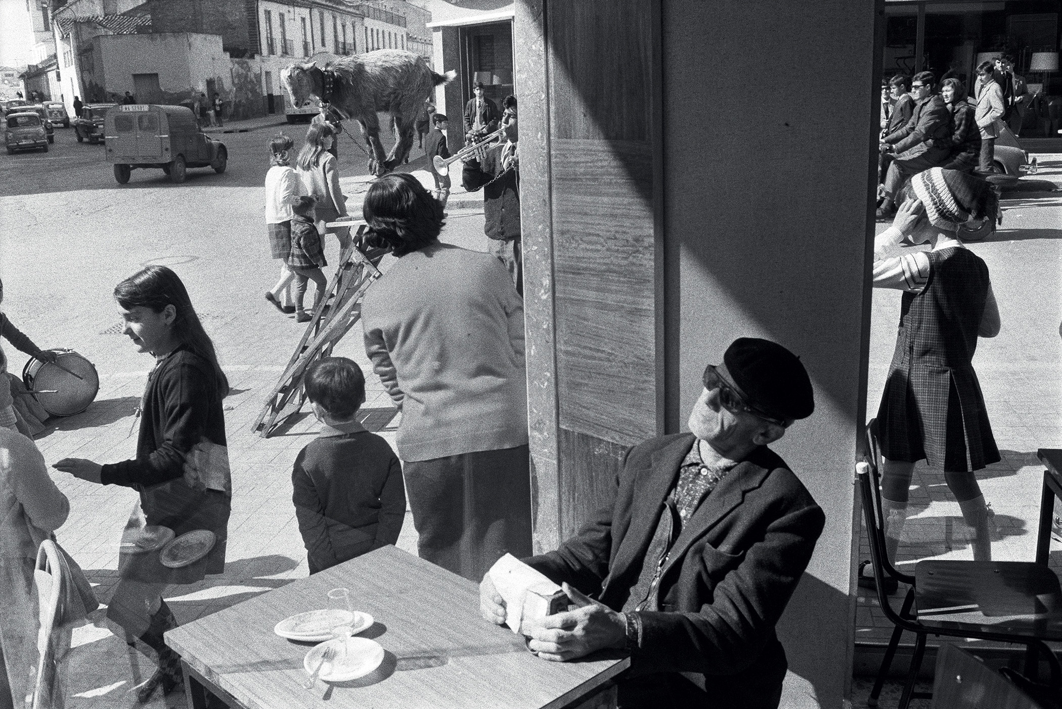 A man in sunglasses sits in a café while crowds of pedestrians are visible through the window